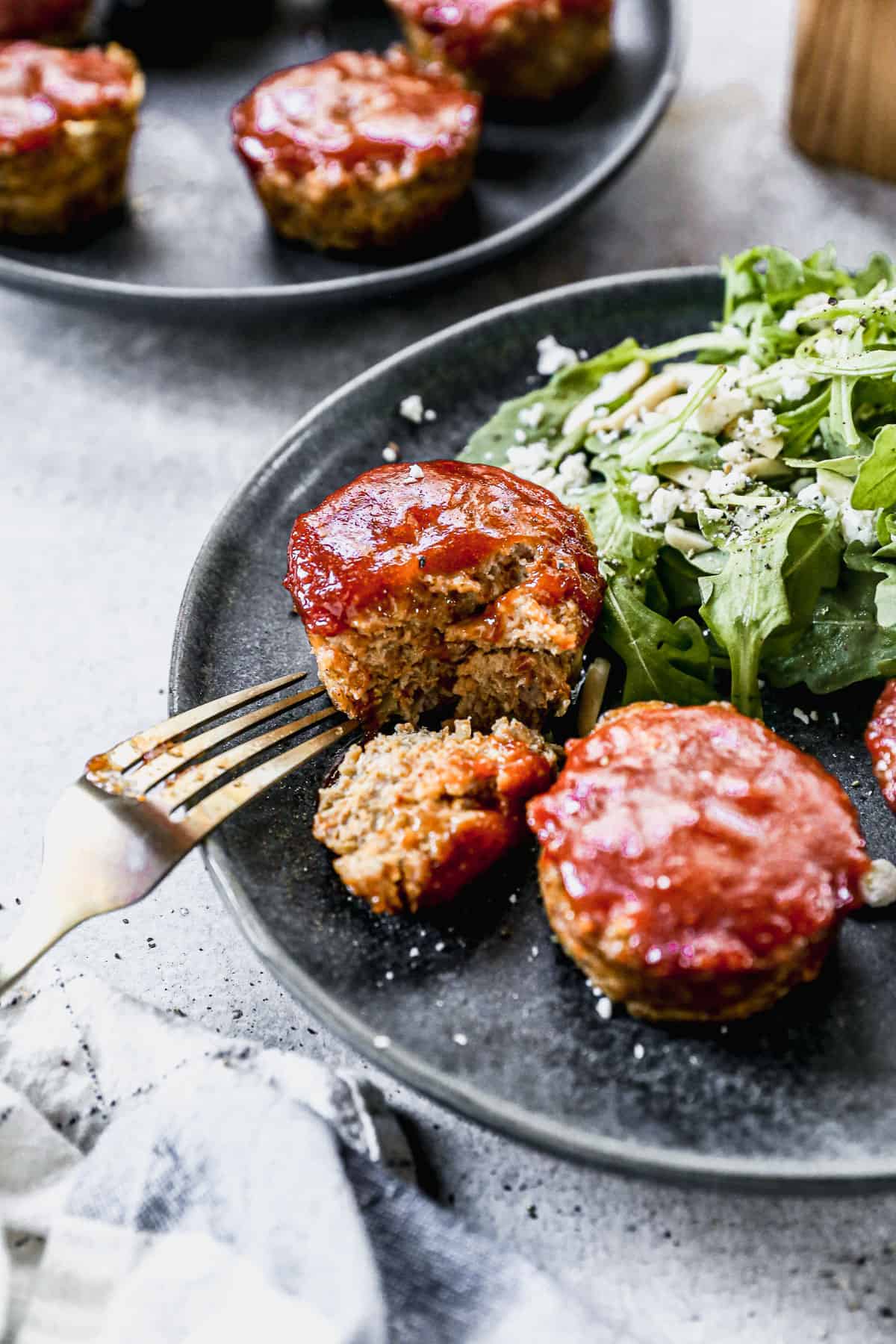 The best mini meatloaf recipe cooked in a muffin tin and topped with a flavorful sauce, served on a plate with a green salad. 