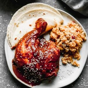 A plate with mole sauce served over chicken with a side of Mexican rice and a tortilla.