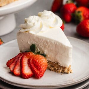 A slice of no bake cheesecake served on a plate, with a sliced strawberry.