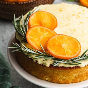 The best Orange Olive Oil Cake recipe topped with a whipped mascarpone frosting, candied orange slices, and rosemary sprigs.