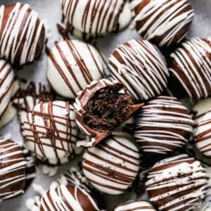 An easy Oreo Balls recipe, some dipped in milk chocolate and some dipped in white chocolate with the opposite chocolate drizzled on top. One of them has a bite out of it to show the creamy center.