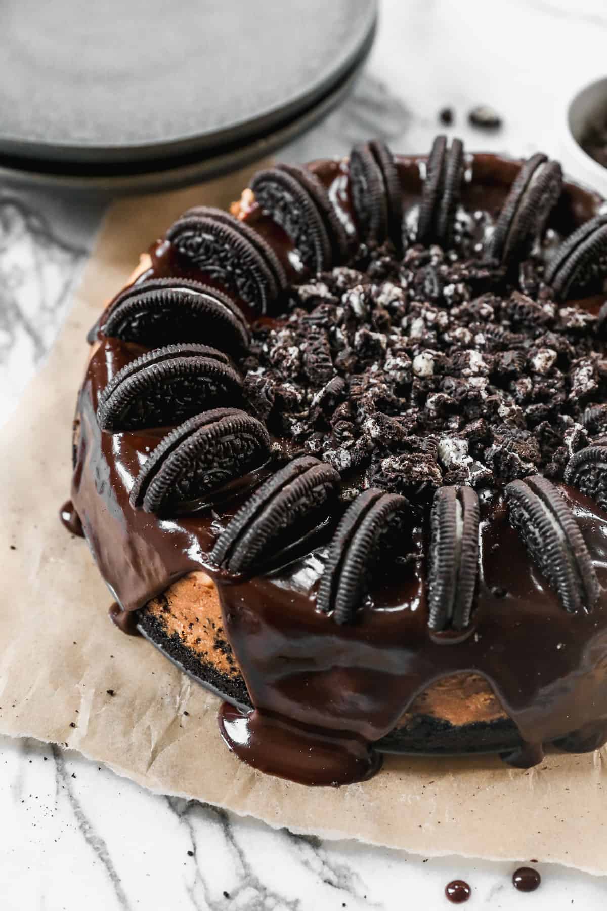 A homemade Oreo Cheesecake covered in chocolate ganache and decorated with Oreos, cut in half around the edges and crushed Oreos in the center.