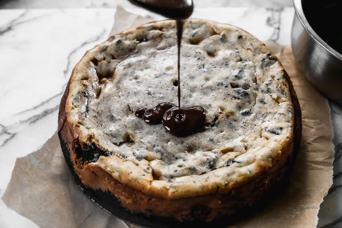 Homemade chocolate ganache being poured on top of a simple Oreo Cheesecake recipe. 