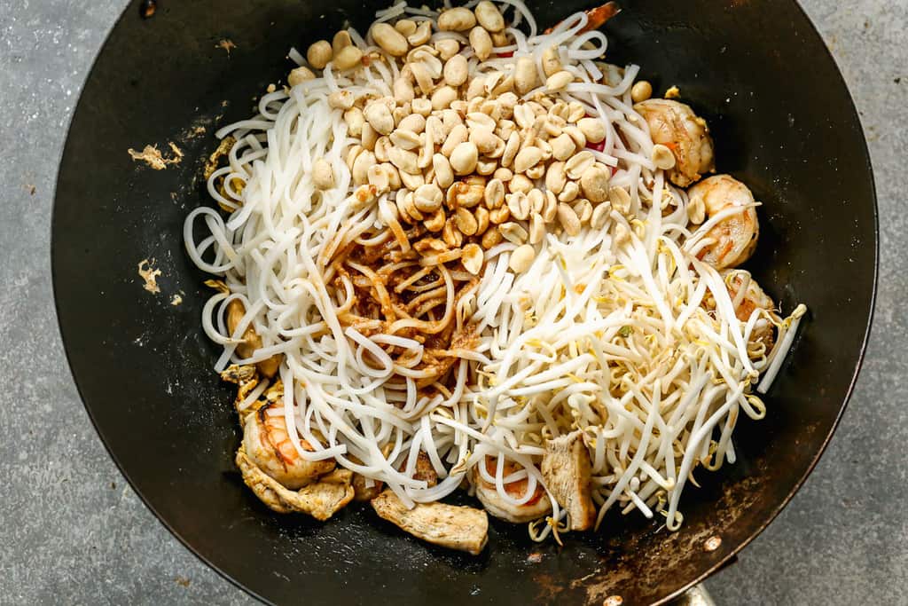 Pad thai noodles and sauce added to a wok with sautéing veggies, chicken and shrimp.