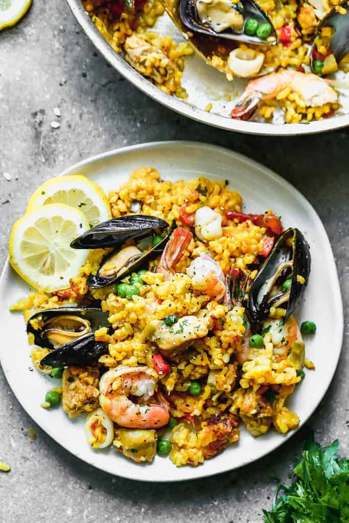 A serving of paella mixta on a plate, with sliced lemons on the side.