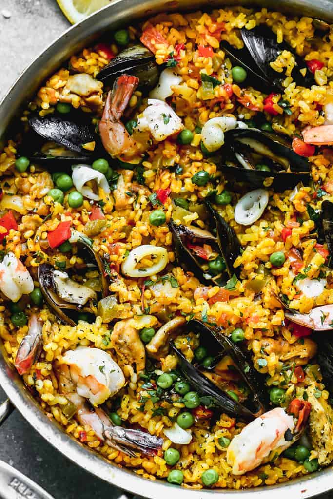 Close up of cooked chicken and seafood paella in pan, ready to eat.