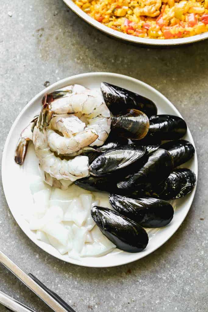 Seafood for paella, including shrimp, mussels and squid, on a plate.