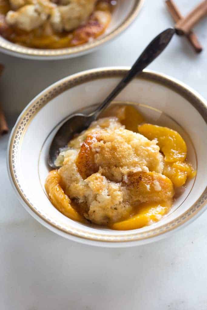 Peach cobbler served in a bowl with a spoon, and another bowl of cobbler in the background.