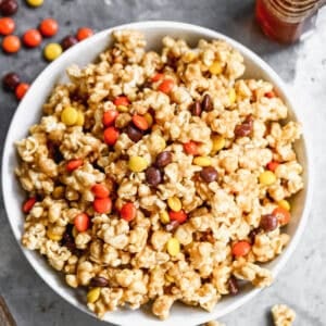 Peanut Butter Popcorn in a large white bowl with Reese's Pieces sprinkled throughout.