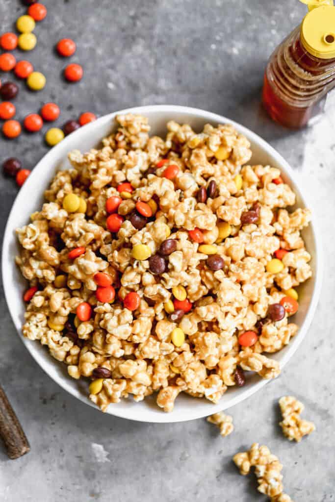 Peanut Butter Popcorn in a large white bowl with Reese's Pieces sprinkled throughout.