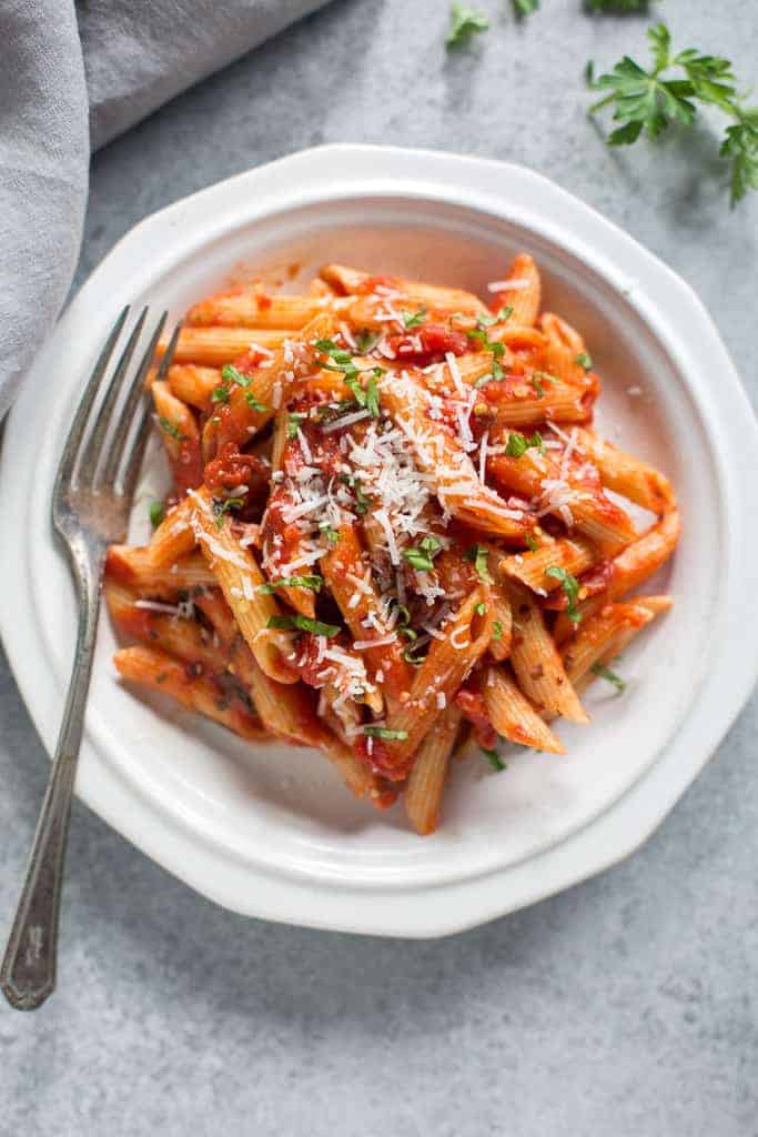 A white plate full of Italian penne arrabbiata garnished with fresh parmesan cheese.