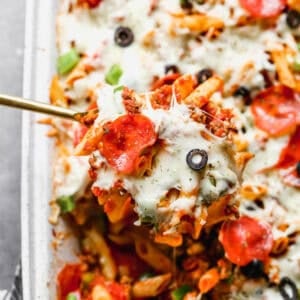 An easy pizza casserole recipe with a scoop being lifted to show the cheesy pasta with pepperoni, olives, bell peppers, and meat.