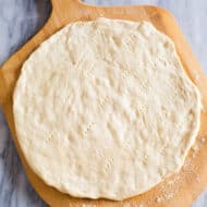 Pizza dough stretched into a round circle and pricked with a fork on a wooden pizza peel.