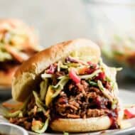 A BBQ pulled pork sandwich with slaw, in a bun, served on a plate.