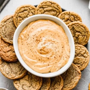 A creamy Pumpkin Pie Dip recipe in a bowl surrounded by a plate of gingersnap cookies.