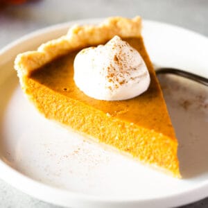 A slice of homemade pumpkin pie with whipped cream.