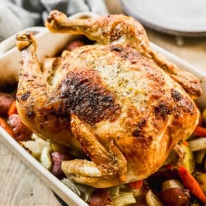 The best Roast Chicken recipe baked to a perfect golden color on top of a bed of potatoes and carrots.