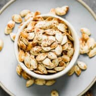 A bowl full of roasted pumpkin seeds with salt and cayenne pepper, cooked until golden brown.