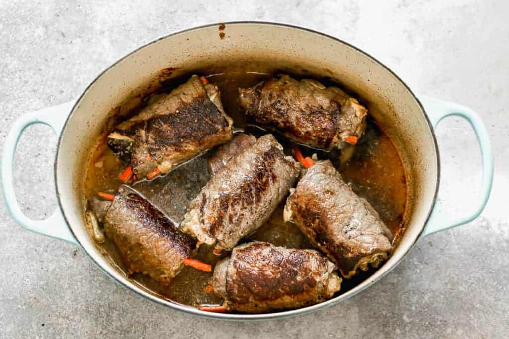 A dutch oven pot with German Rouladen cooking in it.