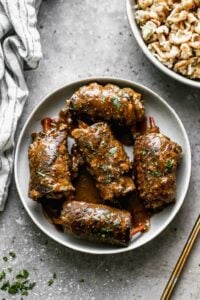 A serving plate with five Beef Rouladen in gravy on it.