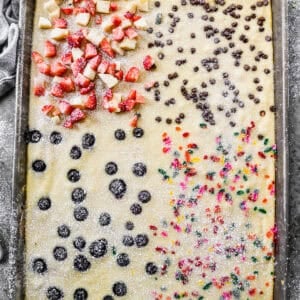 Easy Sheet Pan Pancakes divided into four quarters of flavors: sprinkles, blueberries, mini chocolate chips, and fresh strawberries and bananas.