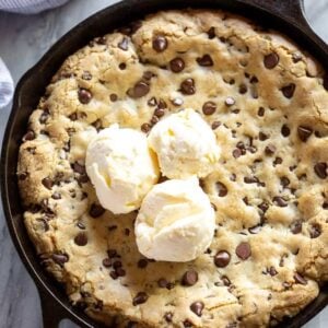 A skillet cookie baked in a cast iron skillet with three scoops of vanilla ice cream on top.