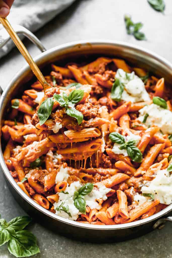 A spoon holding up a serving of skillet lasagna from the pan.