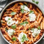 A large pan of cooked Skillet Lasagna, topped with spoonfuls of ricotta and fresh basil.