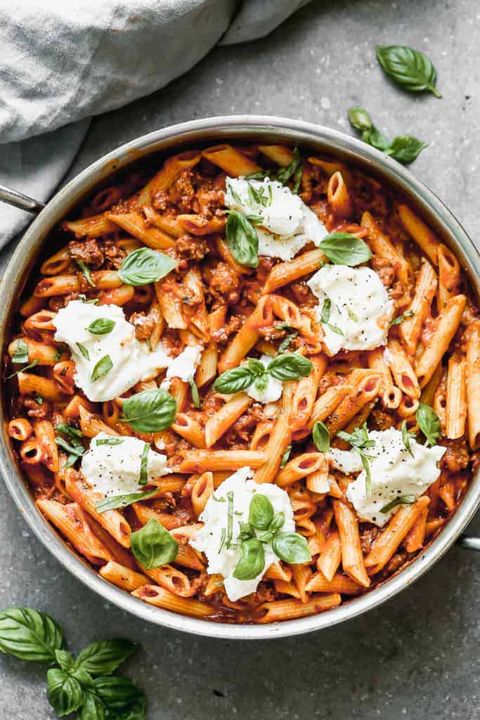 A large pan of cooked Skillet Lasagna, topped with spoonfuls of ricotta and fresh basil.