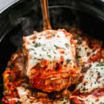 A piece of easy crockpot lasagna being lifted from the slow cooker by a spatula.