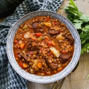 A hearty Spanish Lentil Stew recipe in a bowl with potatoes, veggies, and chorizo.