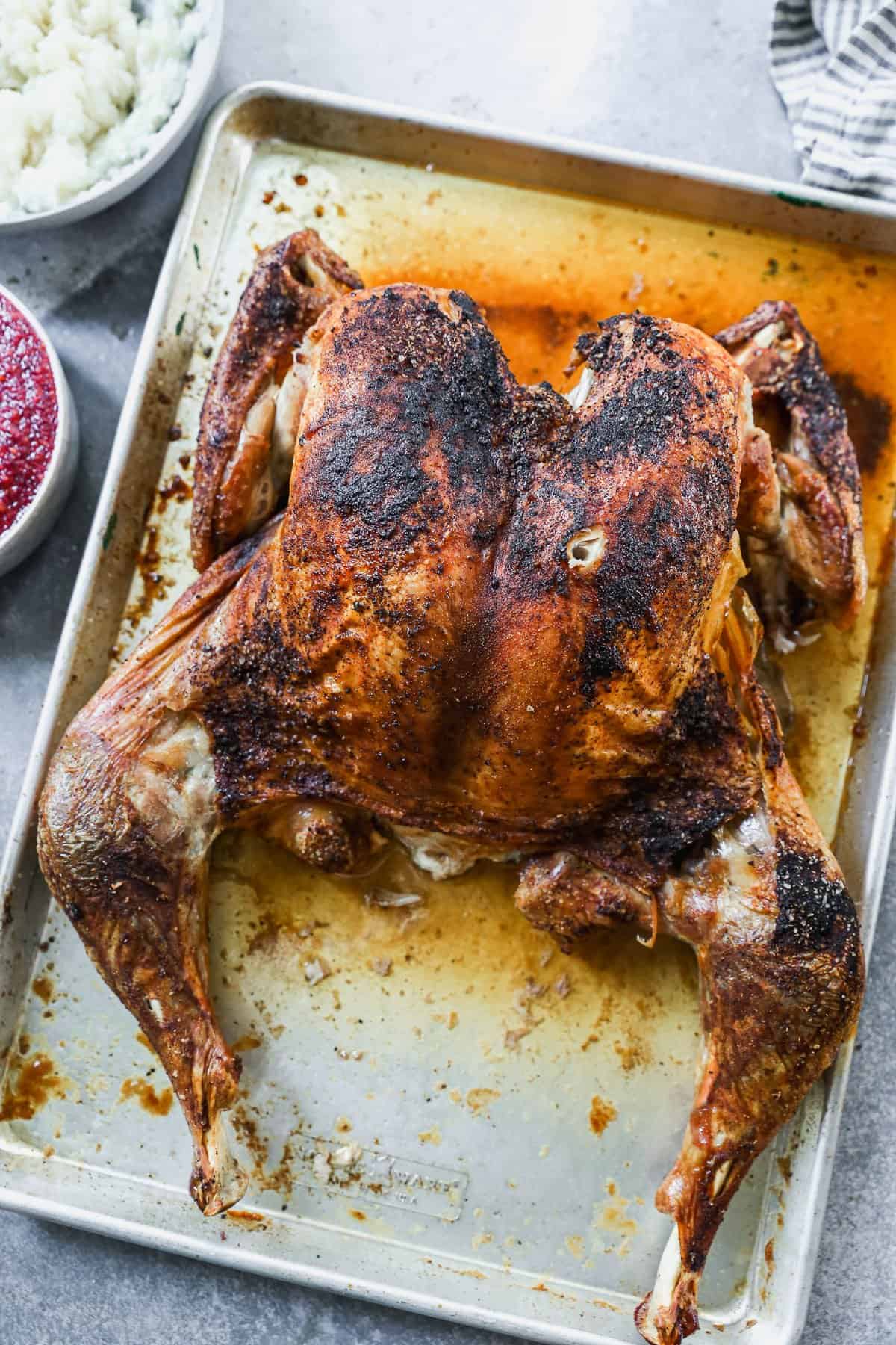 A spatchcocked turkey on a baking sheet, cooked until golden brown and ready to carve. 