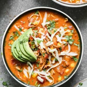 A bowl of Spicy Chicken Soup garnished with sliced avocado and cheese.