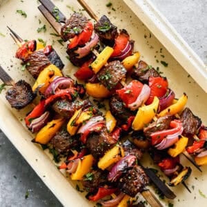 A pan of grilled Steak Kabobs with steak, red and yellow bell pepper, and red onion, ready to serve.