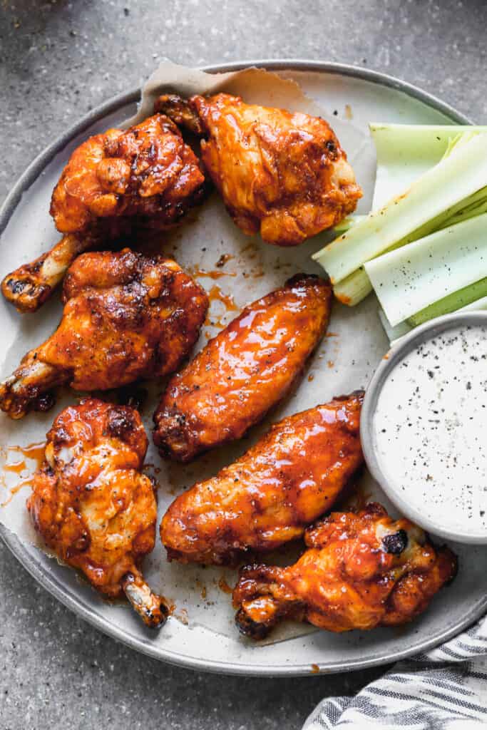 A plate of crispy baked chicken wings served with ranch and celery on the side.