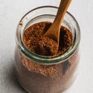 A jar with homemade Taco Seasoning being scooped with a wooden teaspoon.