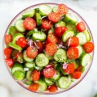 A bowl with chopped tomato, cucumber, onion and basil to make tomato cucumber salad.