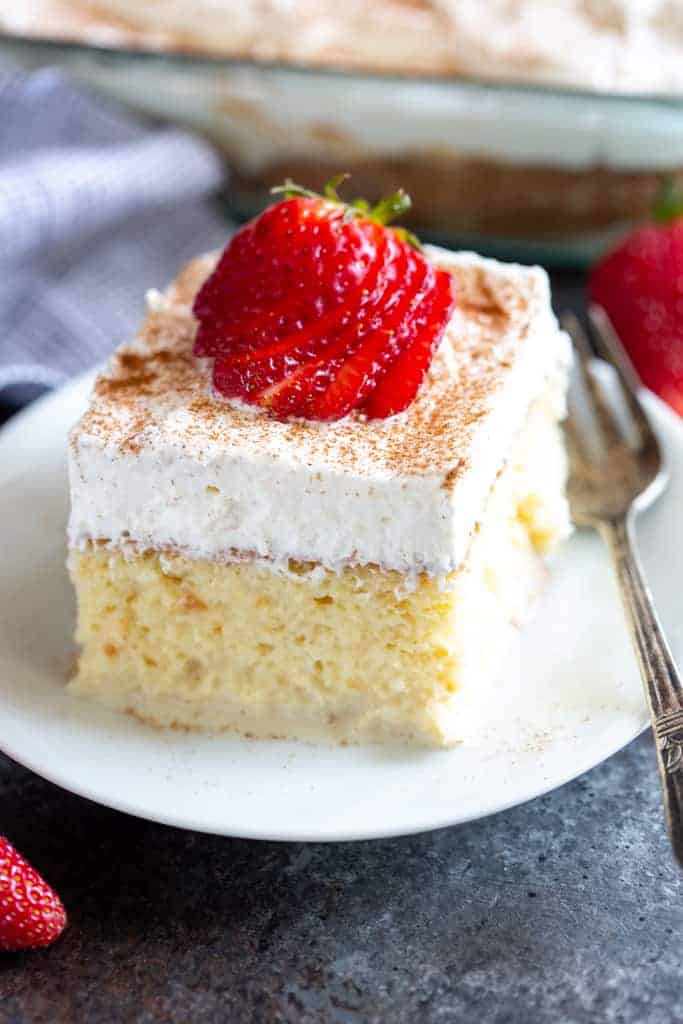 A slice of Tres Leches Cake with a sliced strawberry on top, served on a plate.