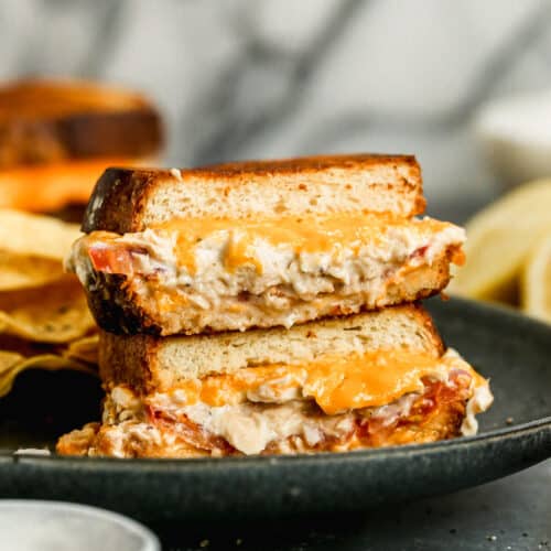 Two halves of a tuna melt sandwich stacked on each other, on a plate.