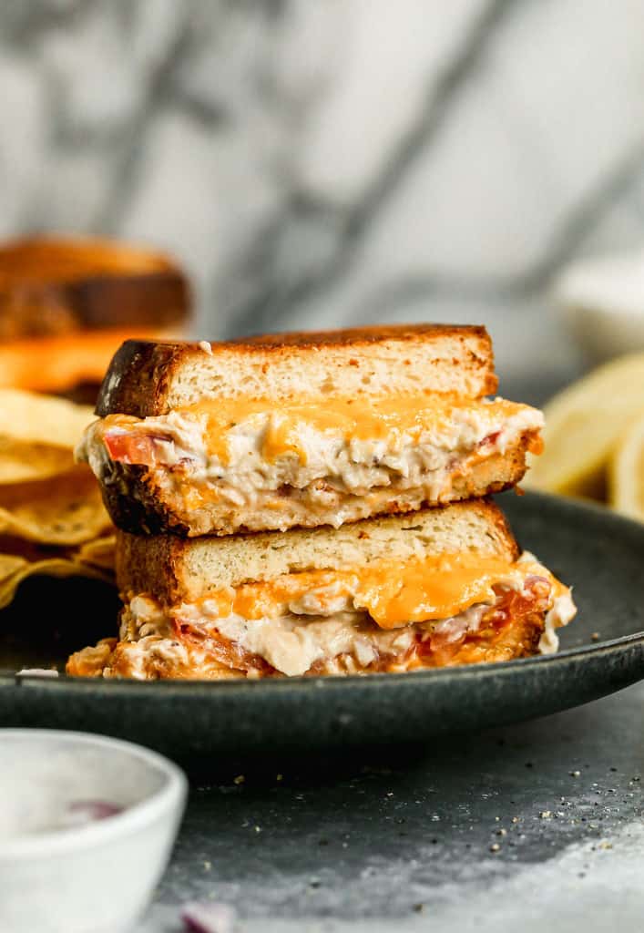 Two halves of a tuna melt sandwich stacked, on a plate.