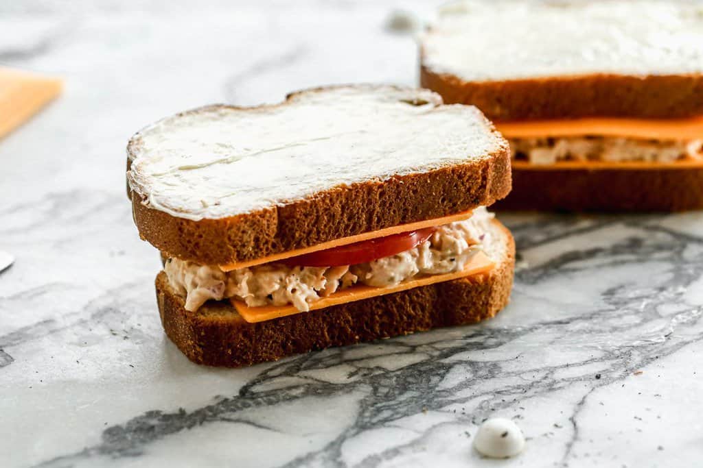 Assembled tuna sandwich with buttered bread tops, ready to be toasted.