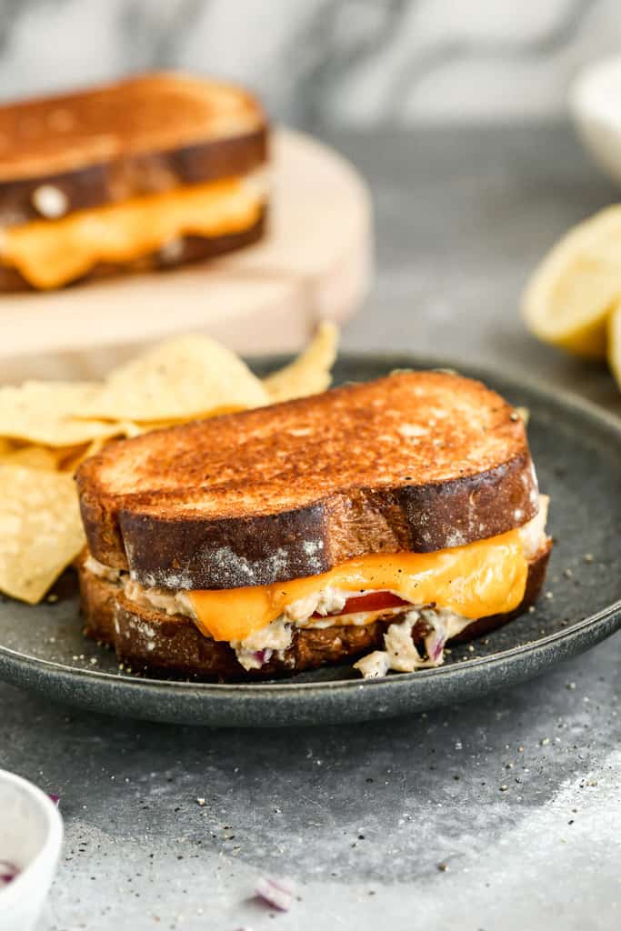 Warm toasted tuna melt served on a plate with potato chips on the side.