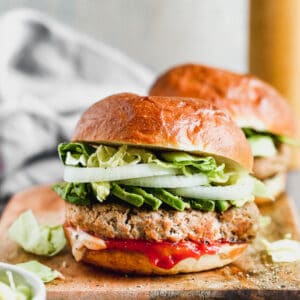 Two turkey burgers served in buns, topped with avocado, lettuce and onion.