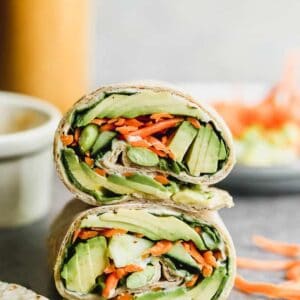 Two veggie wraps stacked on each other, filled with avocado, carrots, hummus and edamame.