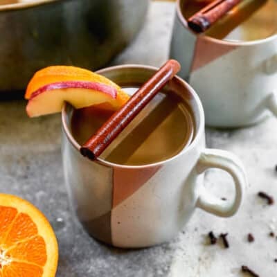 A mug of hot Wassail, with a cinnamon stick, apple slice, and orange slice on top of the mug.