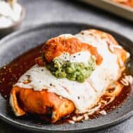 A wet burrito on a plate smothered in enchilada sauce and melted cheese.