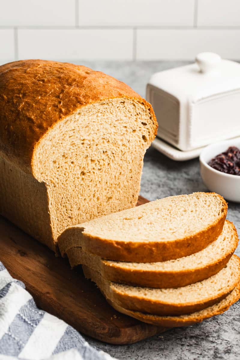 The best whole wheat bread recipe on a cutting board with four slices freshly cut and ready to enjoy with butter and jam. 